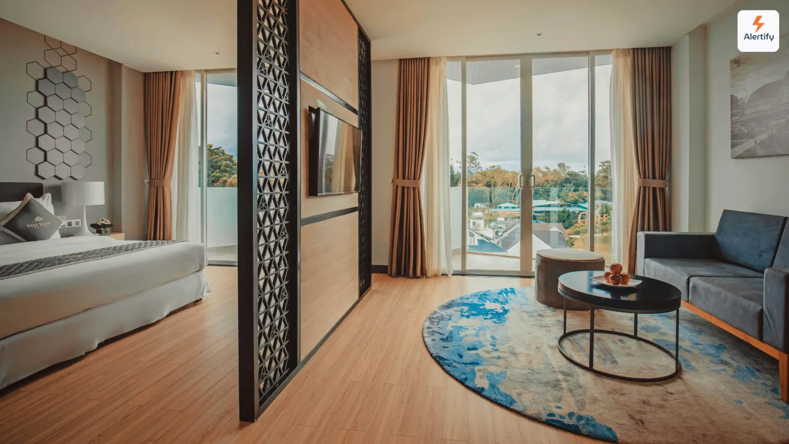 Suite de location de courte durée moderne avec un lit fait, un canapé bleu et des baies vitrées donnant sur un balcon