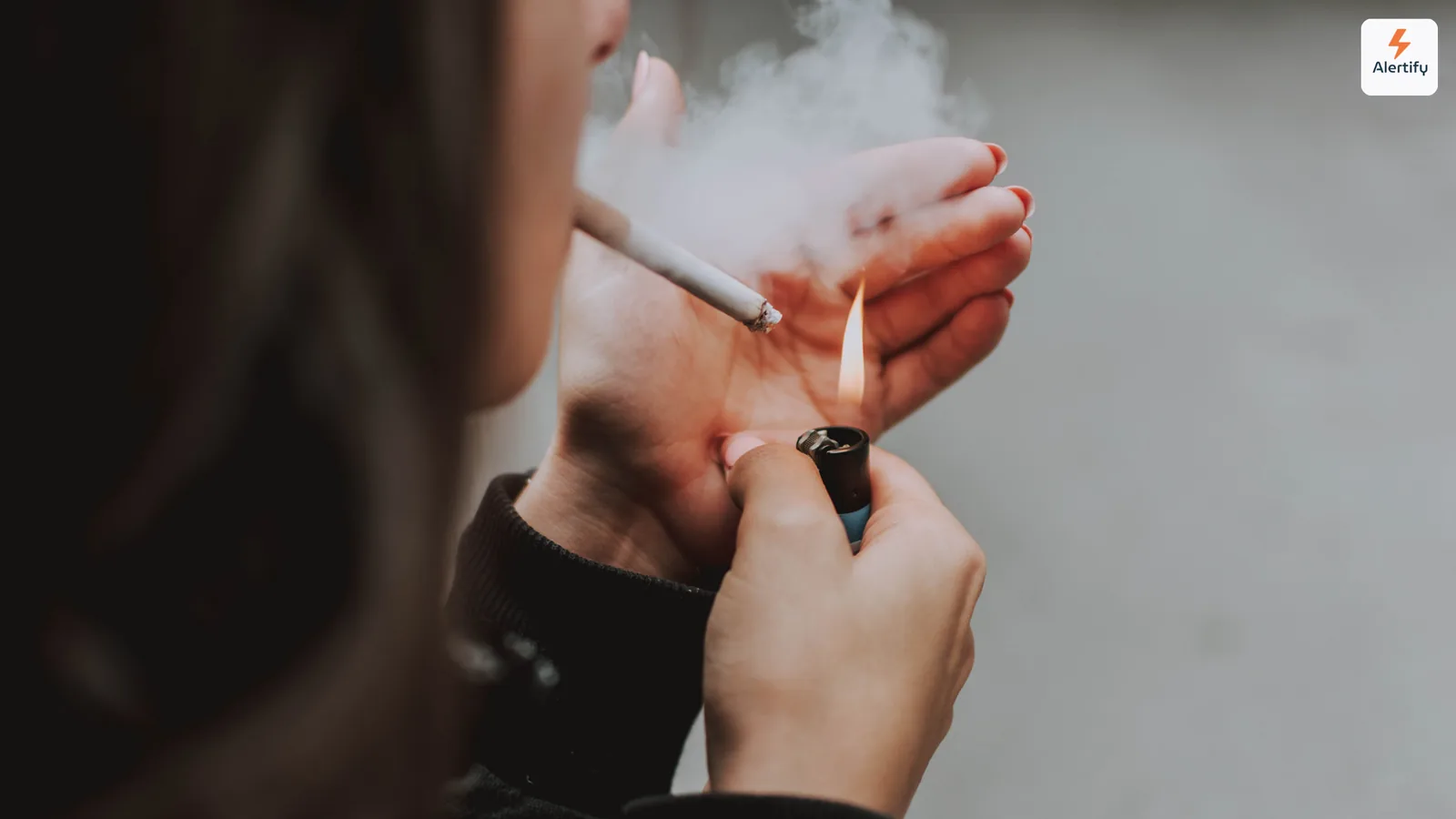 Personne allumant une cigarette à l'intérieur, avec de la fumée s'enroulant autour de ses mains