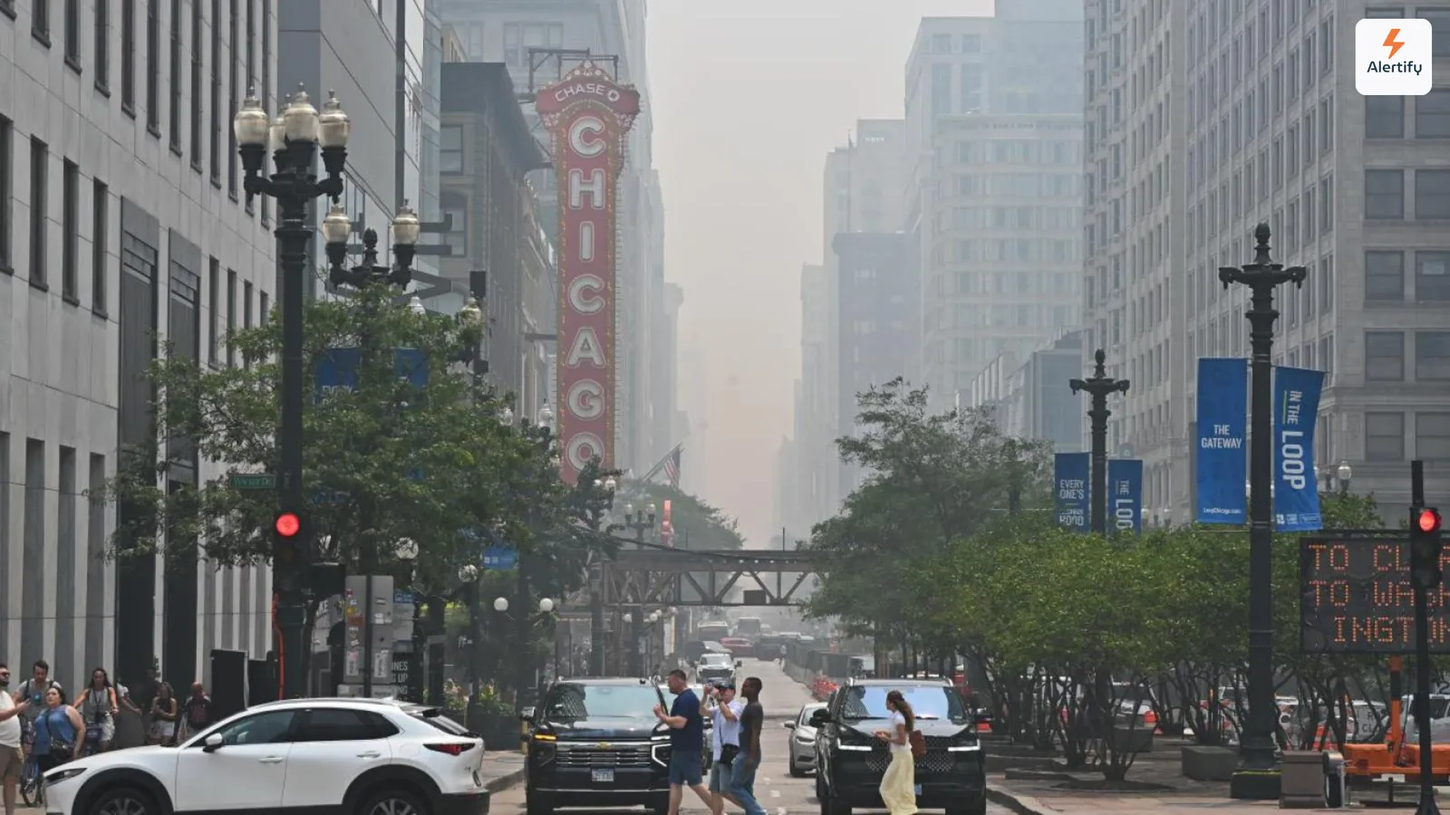 Une brume de fumée d'incendie engloutissant les immeubles d'une rue de Chicago, avec l'enseigne allumée du Chicago Theatre au premier plan.