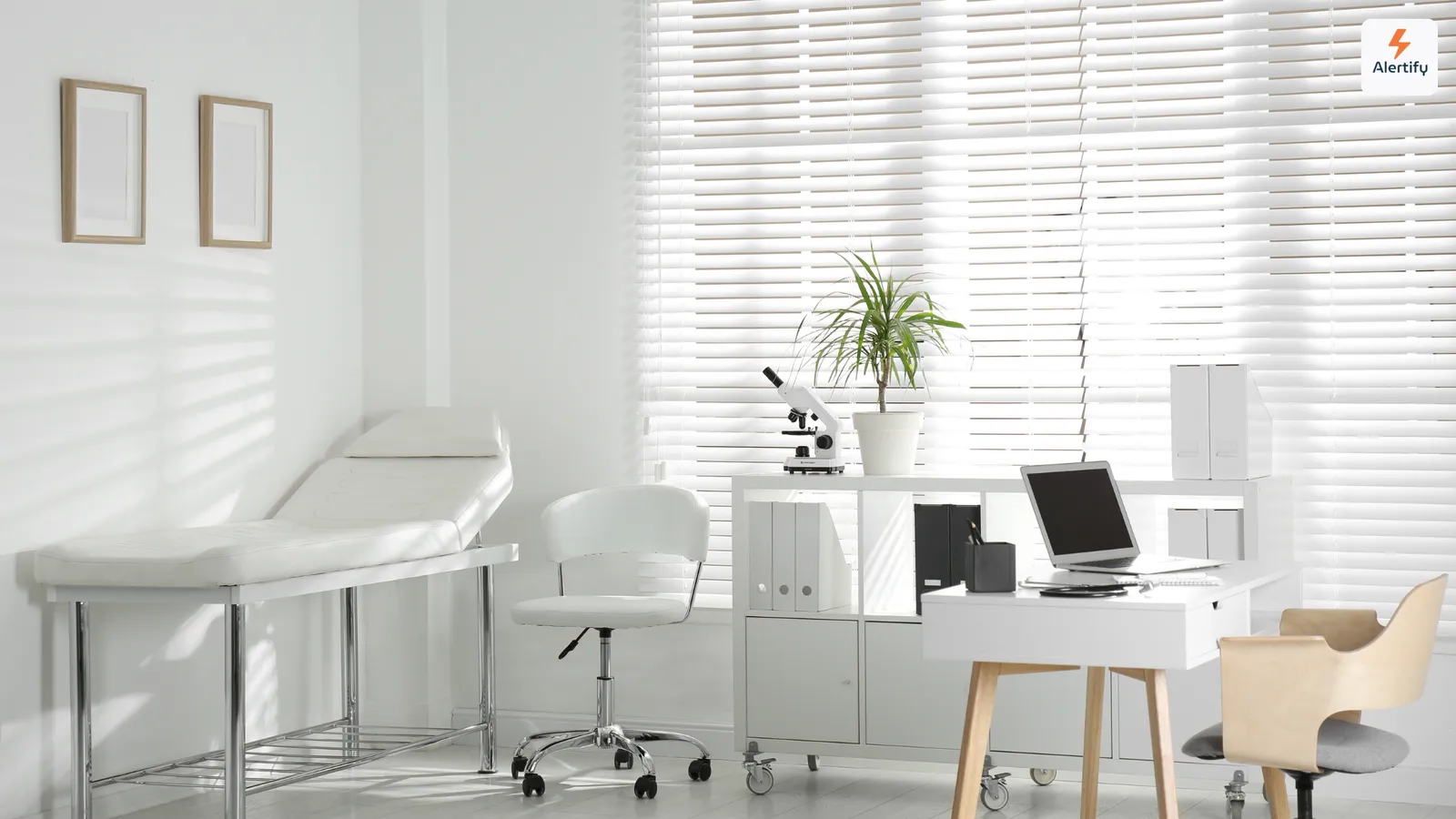 Salle de consultation vide avec une table d'examen, un bureau avec un ordinateur portable et des stores aux fenêtres