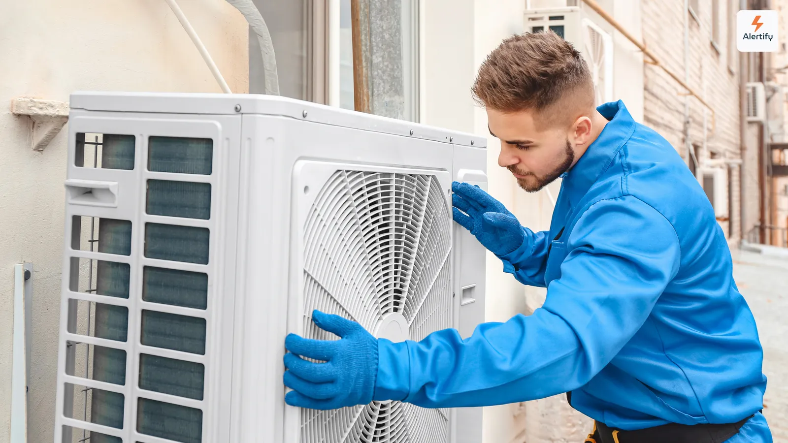 Technicien CVC en combinaison bleue et gants intervenant sur une unité extérieure de climatisation
