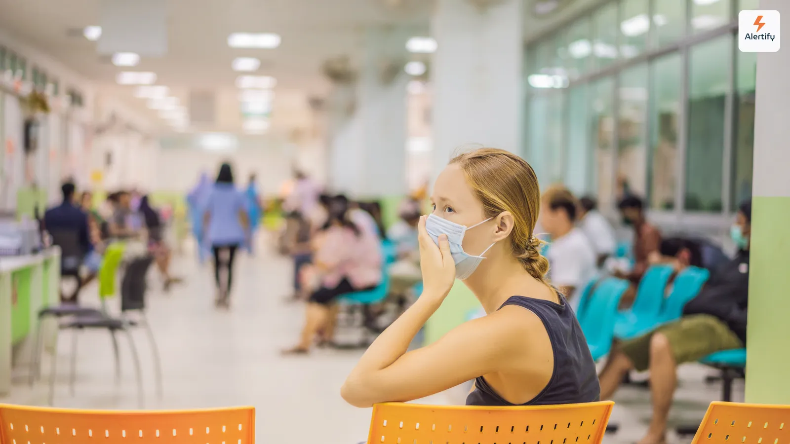 Femme portant un masque, assise dans une salle d'attente d'hôpital très fréquentée