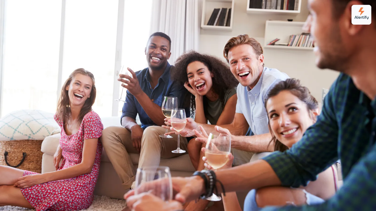 Groupe d'amis riant en trinquant avec des verres de vin dans le salon d'une location de vacances