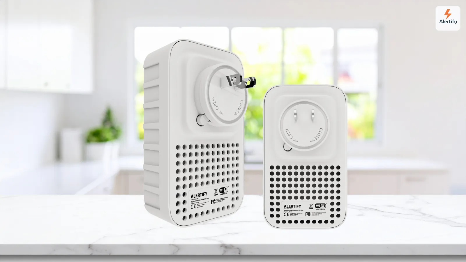 Deux dispositifs de surveillance Alertify à brancher, le plus grand adapté à l'extérieur et le plus petit pour l'intérieur, côte à côte sur un plan de travail de cuisine.