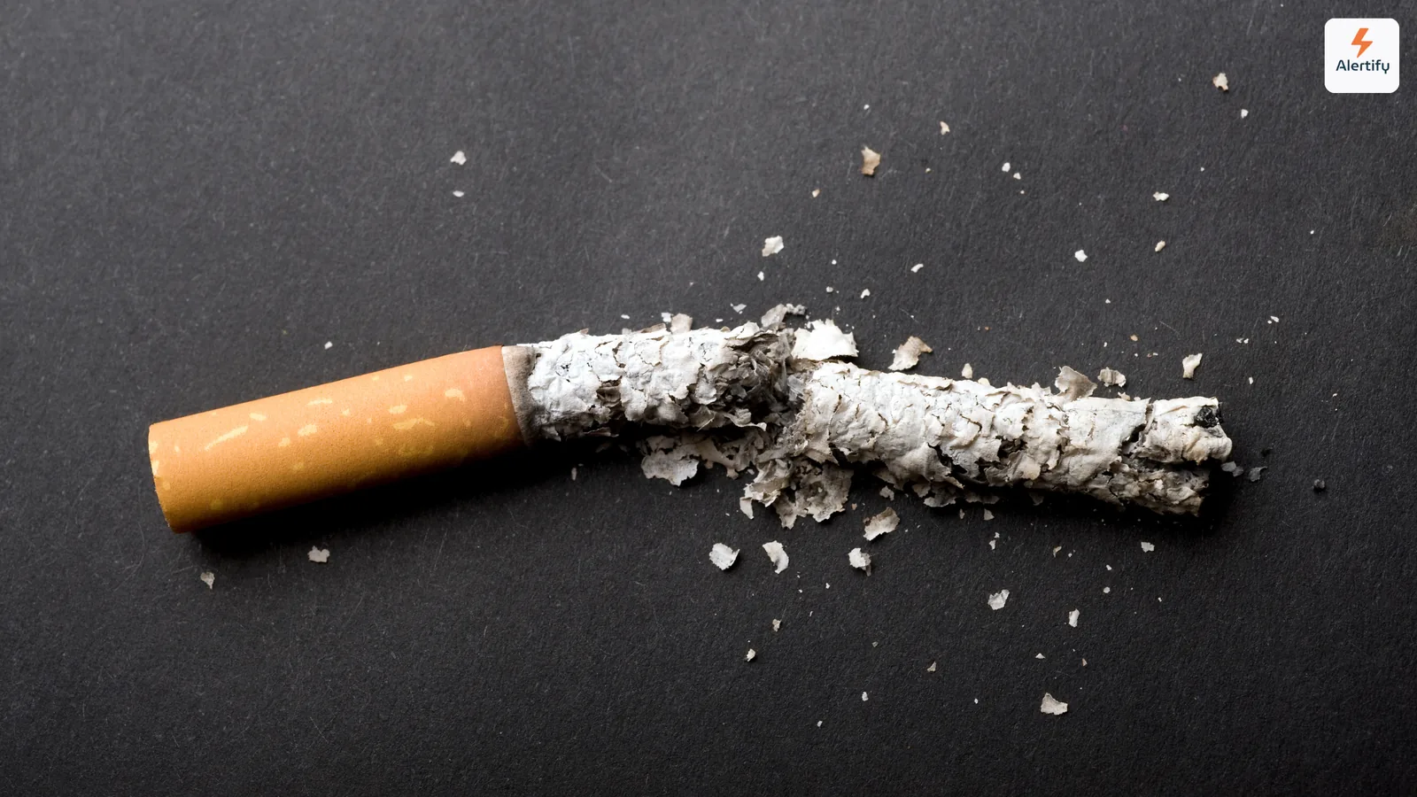 Cigarette brisée en deux avec des cendres éparpillées sur une surface sombre